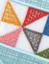 Close-up of a colorful embroidered textile pattern featuring six triangular sections in orange, red, pink, brown, blue, and green on a white mesh background with a light blue stitched border.