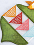 A close-up of a colorful embroidered patch featuring geometric triangles in green, orange, red, pink, and light blue on a white mesh background.