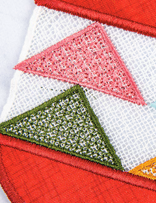 Close-up of a textile or rug featuring a geometric pattern with red borders, a pink triangle, a green triangle, and a white mesh-like center.