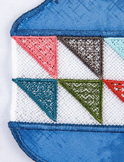 Close-up of a decorative embroidered patch featuring a geometric pattern of triangular flags in pink, brown, teal, green, and red on a white mesh background, bordered by blue embroidered fabric.