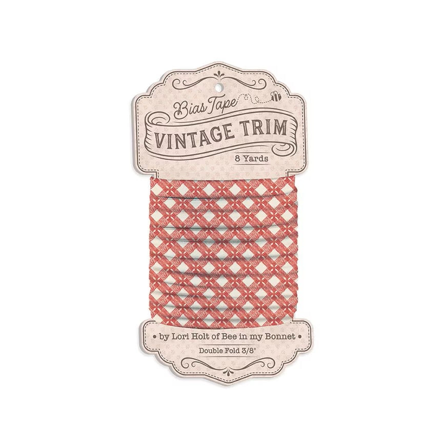 A spool of Bias Tape Vintage Trim ribbon in a red and white lattice pattern, mounted on a decorative beige paper hanger card.