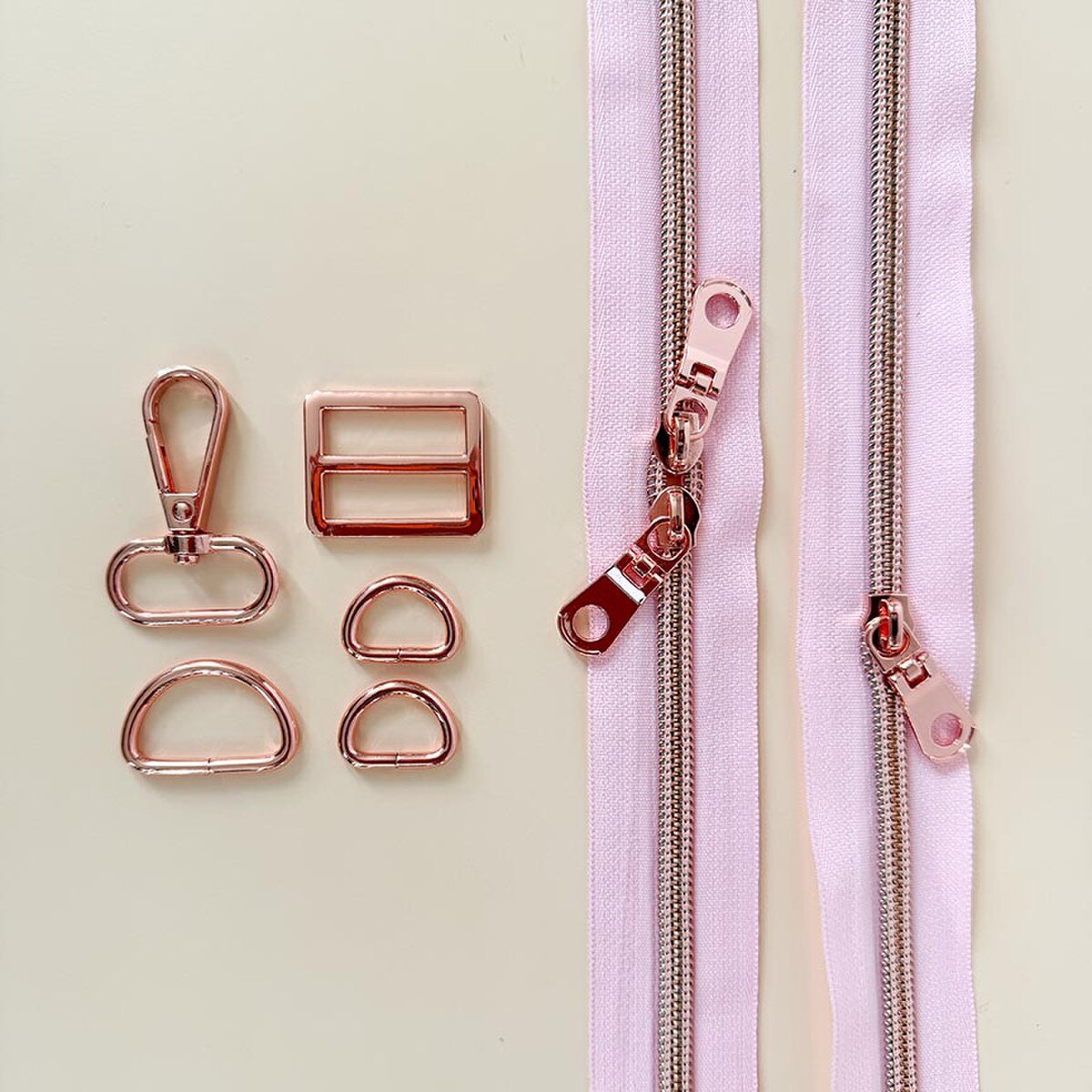 Rose gold zipper pull and hardware components on a light pink zipper background