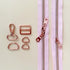 Rose gold zipper pull and hardware components on a light pink zipper background
