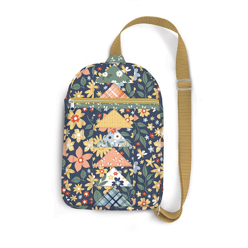A small crossbody bag with a navy blue background and a colorful floral and patchwork-style print, featuring a tan adjustable shoulder strap and a front zip pocket.
