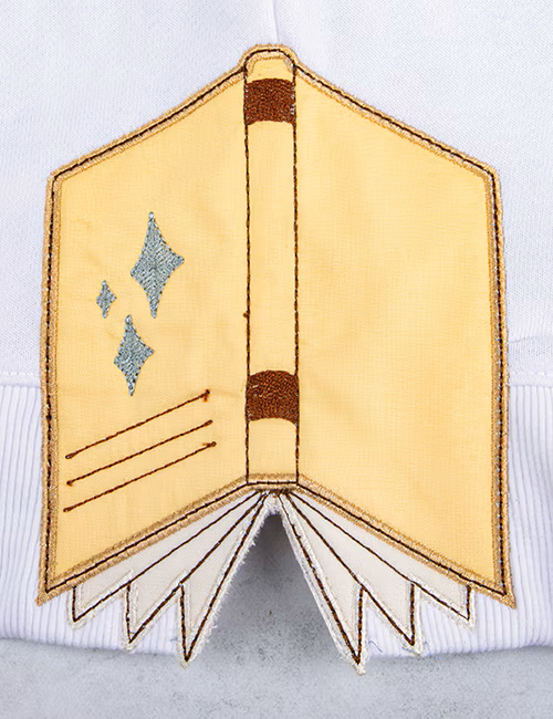 Embroidered patch of an open book with stars on a white background