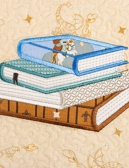 Embroidered design of books with a dragon on top, on a beige background with decorative elements.