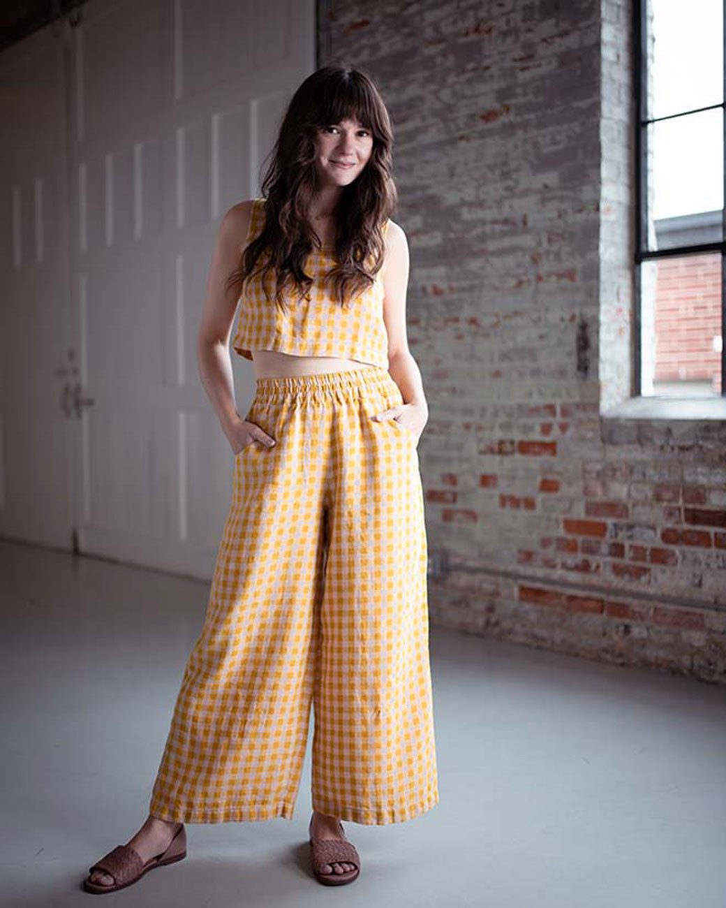 Woman wearing a yellow checkered outfit in an indoor setting with brick walls.