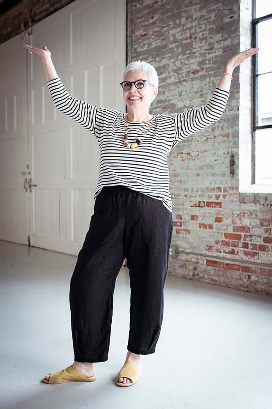Person wearing a striped shirt and black pants in an indoor setting with brick wall and white door.
