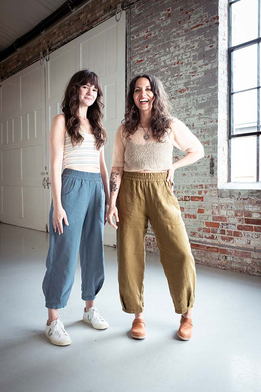 Two women standing in a room with brick walls and large windows.