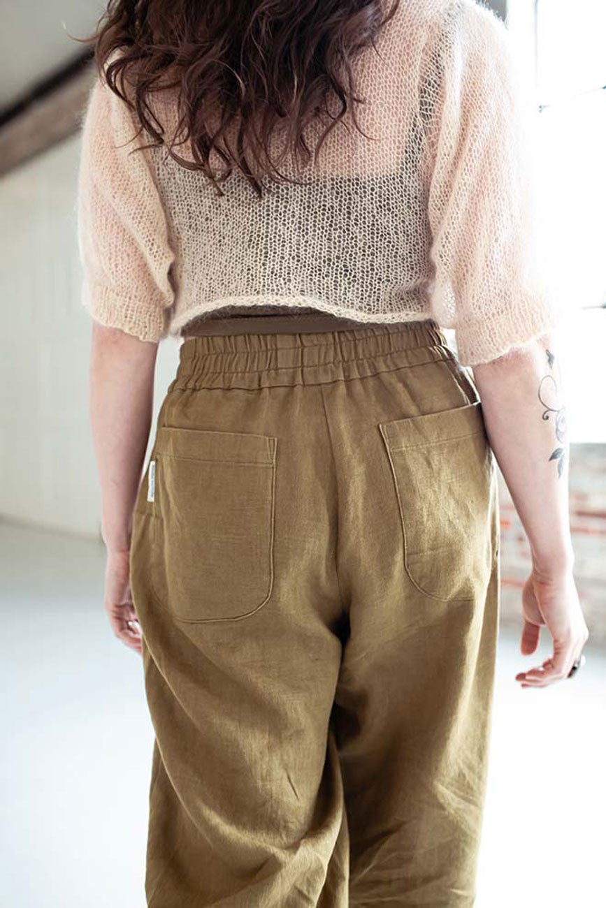 Person wearing a beige knit top and brown pants in a minimal indoor setting