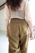 Person wearing a beige knit top and brown pants in a minimal indoor setting