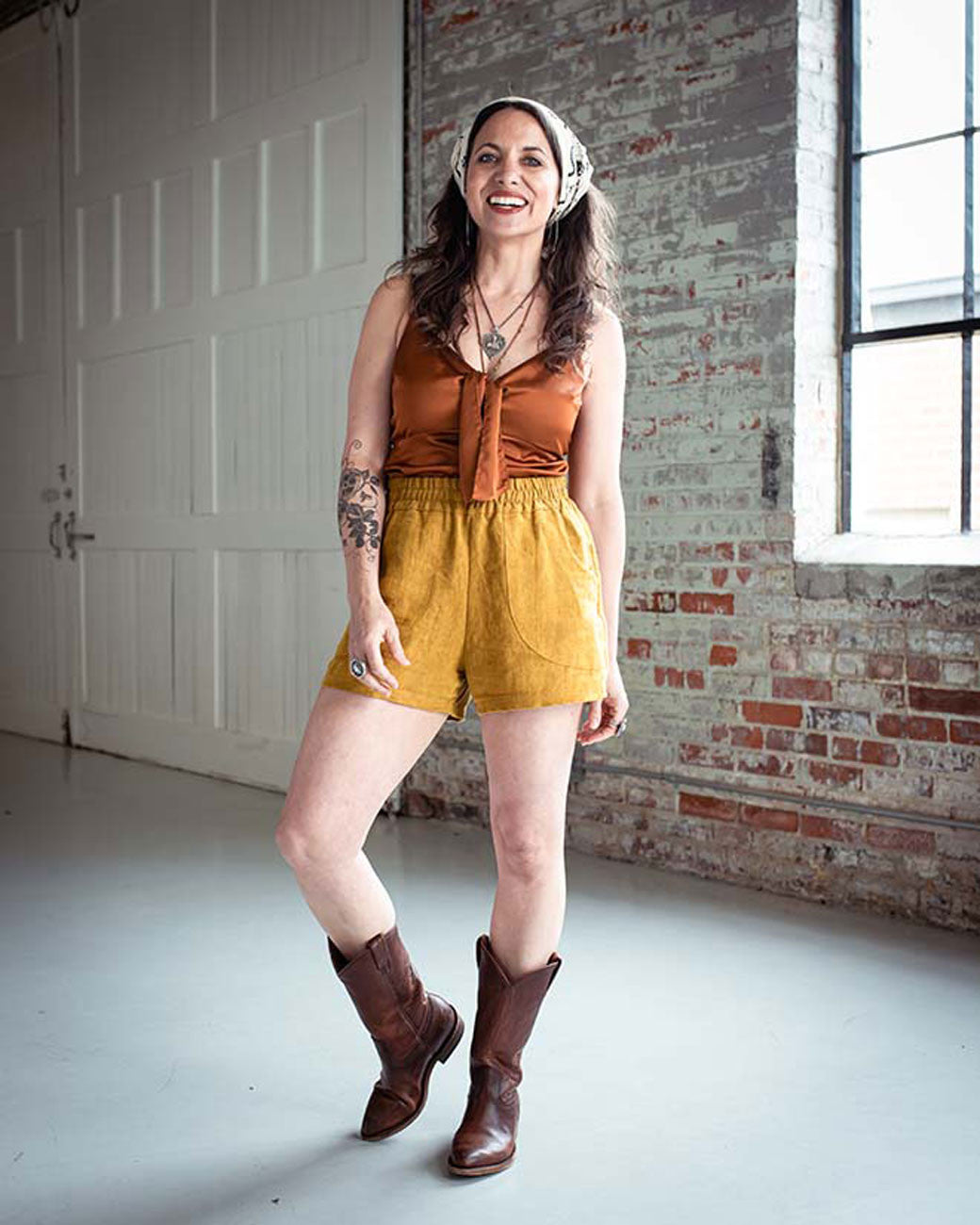 Woman wearing a rust-colored top and yellow shorts with brown boots in an indoor setting.