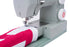 A close-up of a light gray sewing machine with a red and white quilted fabric piece being fed under the needle, shown on a clean white background.