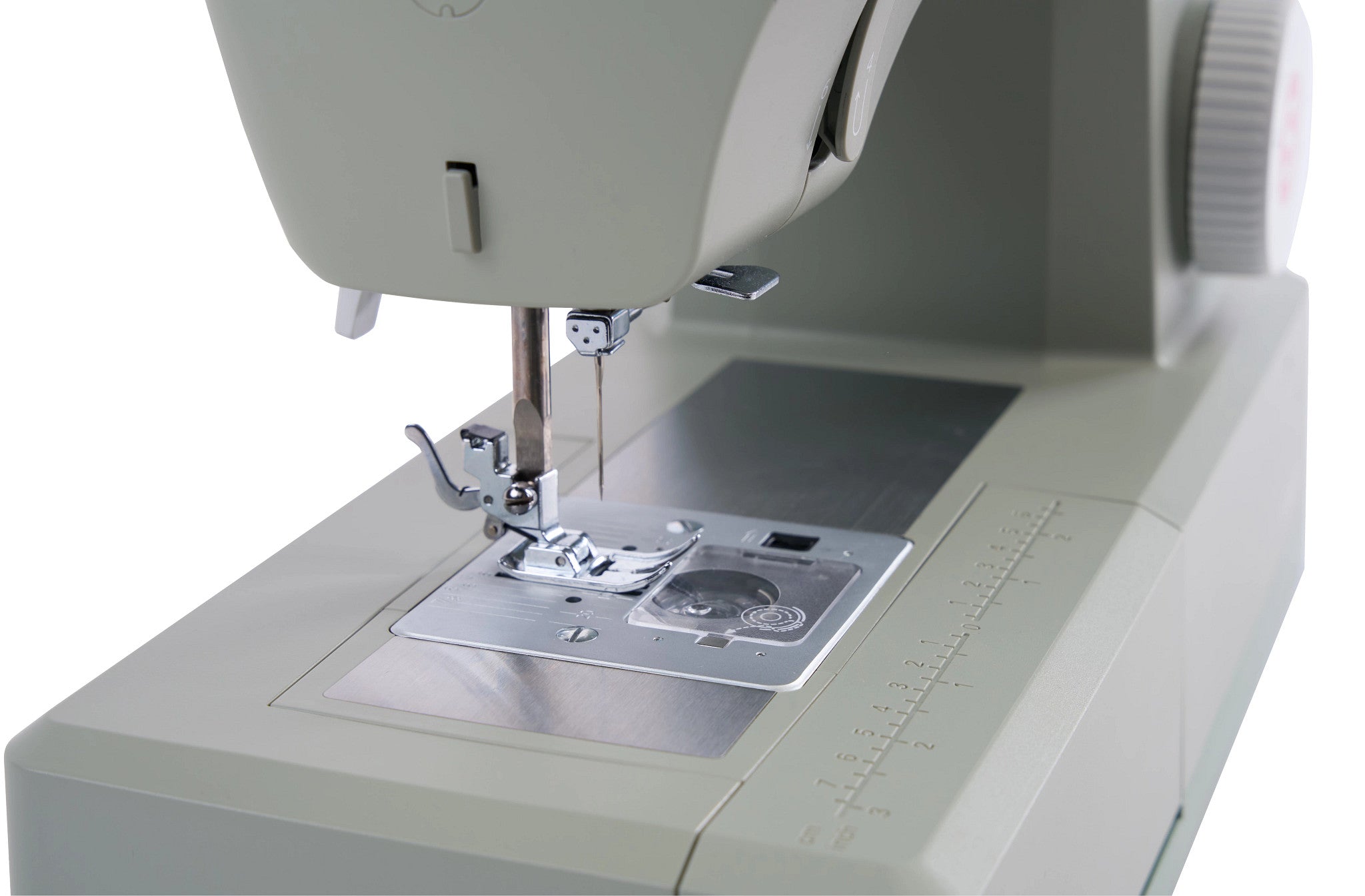 A close-up shot of a sewing machine head and needle area, showing the presser foot, needle, fabric feed dog, and metallic needle plate against a clean white background.