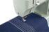 Close-up of a light gray sewing machine stitching dark navy fabric with white zigzag stitch lines on a white background.