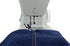 Close-up of a sewing machine stitching dark blue denim fabric with a visible orange-yellow contrast stitch on a white background.