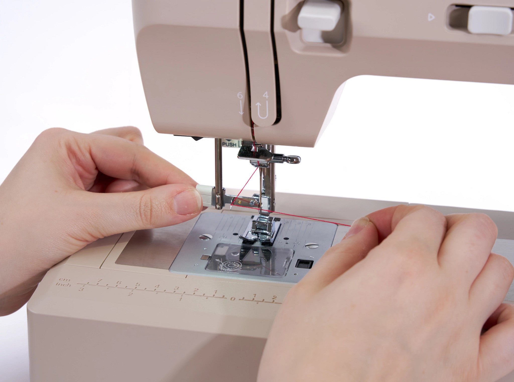Close-up of a person's hands guiding fabric under the needle of a beige sewing machine.