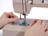 Close-up of a person's hands guiding fabric under the needle of a beige sewing machine.
