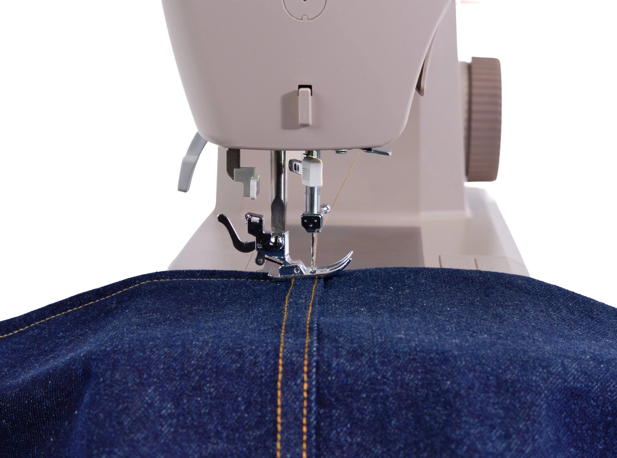 Close-up of a sewing machine stitching a dark blue denim garment, showing the needle, presser foot, thread, and orange contrast stitching against a white background.