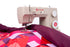 A beige Singer Hilary Daily sewing machine actively sewing a colorful patchwork quilt with a deep purple fabric layer, shown against a solid white background.