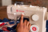 A close-up of a beige Singer Heavy Duty sewing machine with a person's hand adjusting a switch, with fabric visible underneath.