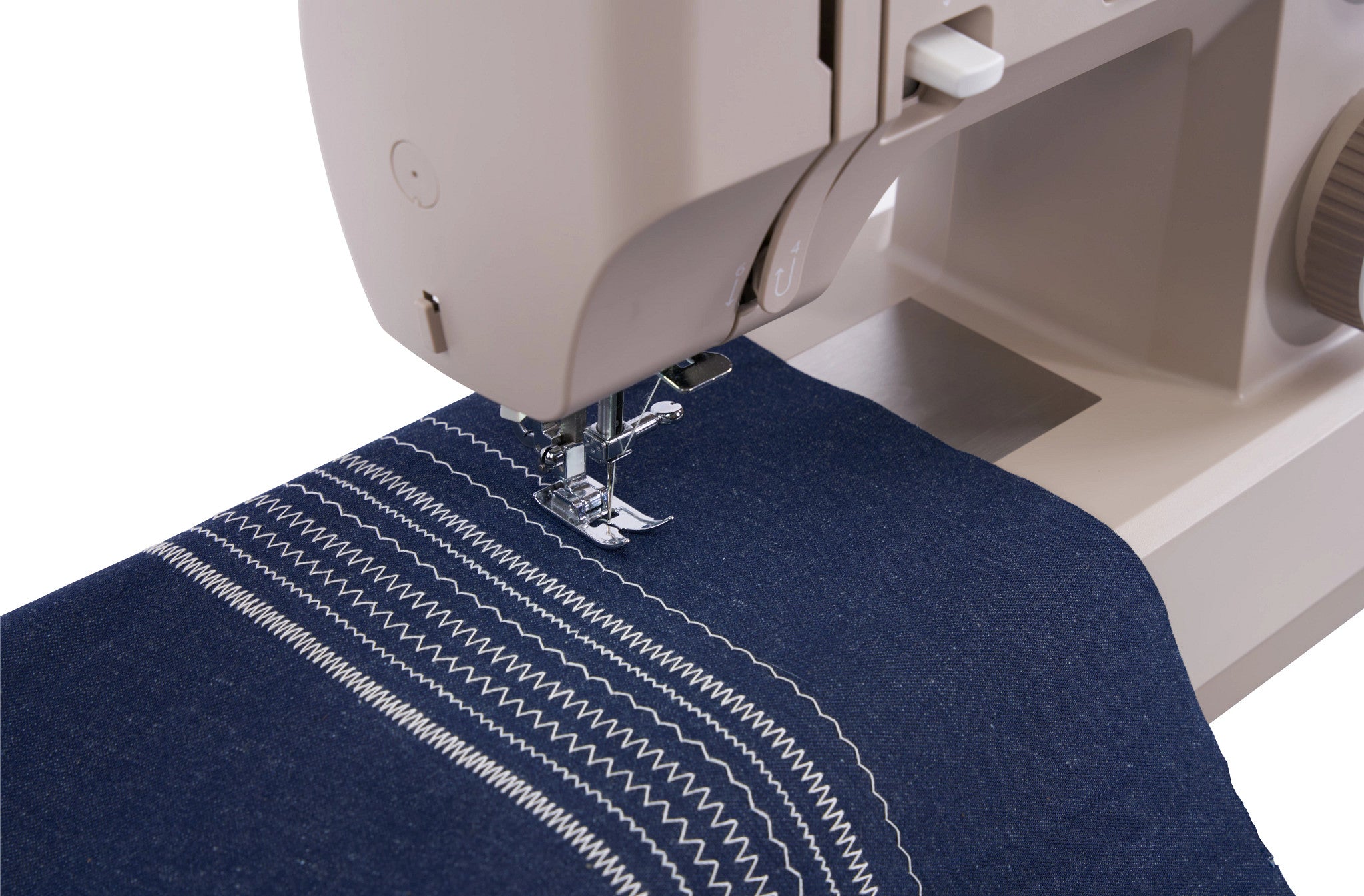 Close-up of a sewing machine stitching a navy blue fabric piece with white zigzag and straight stitch patterns, shown against a white background.
