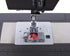 Close-up of a sewing machine needle plate area with a clear cover over a red spool of thread, mounted on a dark gray machine bed with a silver metal plate and ruler markings.