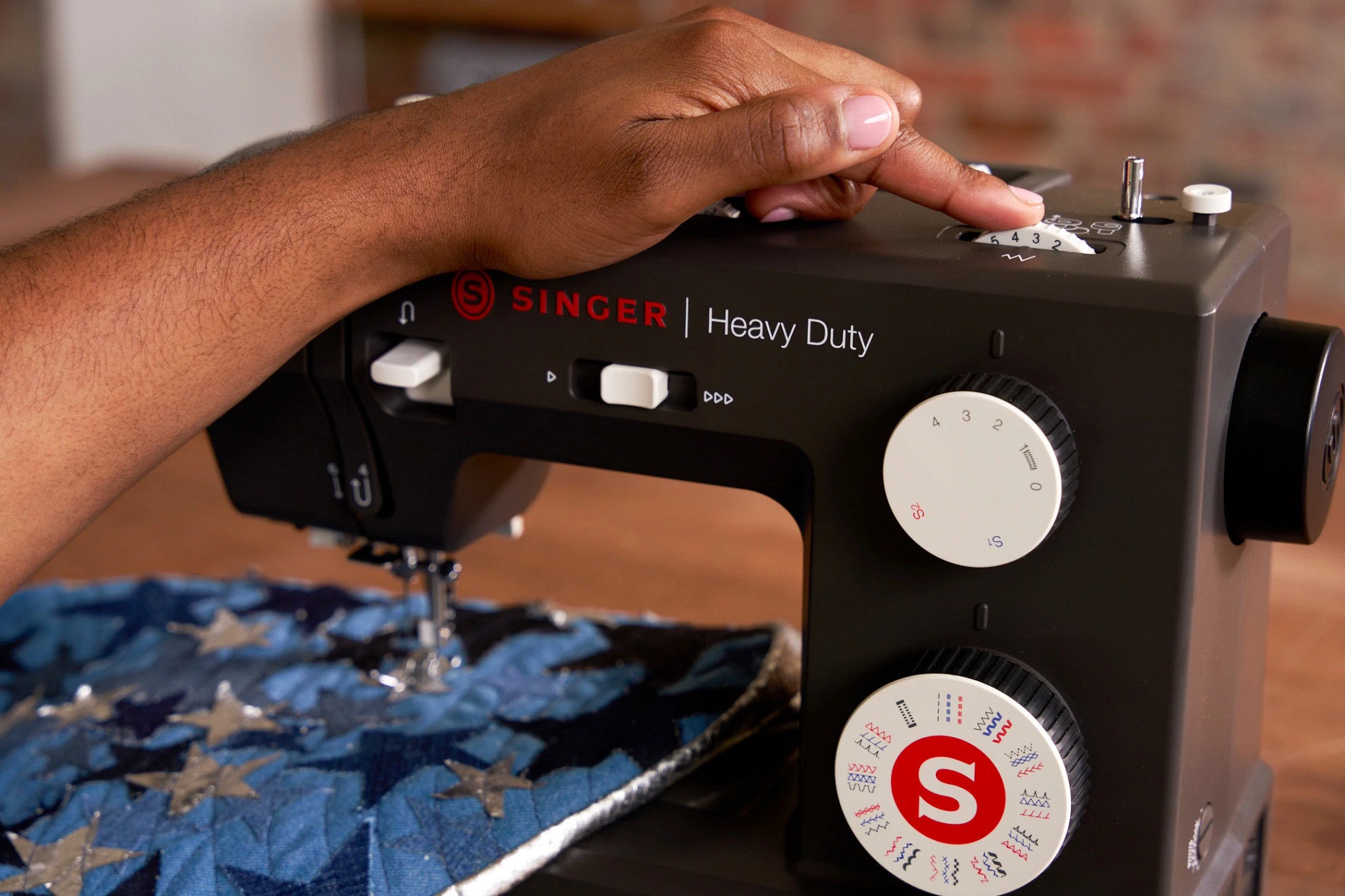 A close-up of a person's hand operating a black Singer Heavy Duty sewing machine, stitching blue patterned fabric.
