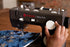 A close-up of a black Singer Heavy Duty sewing machine being operated by a person's hand, with blue fabric featuring silver star patterns under the needle.