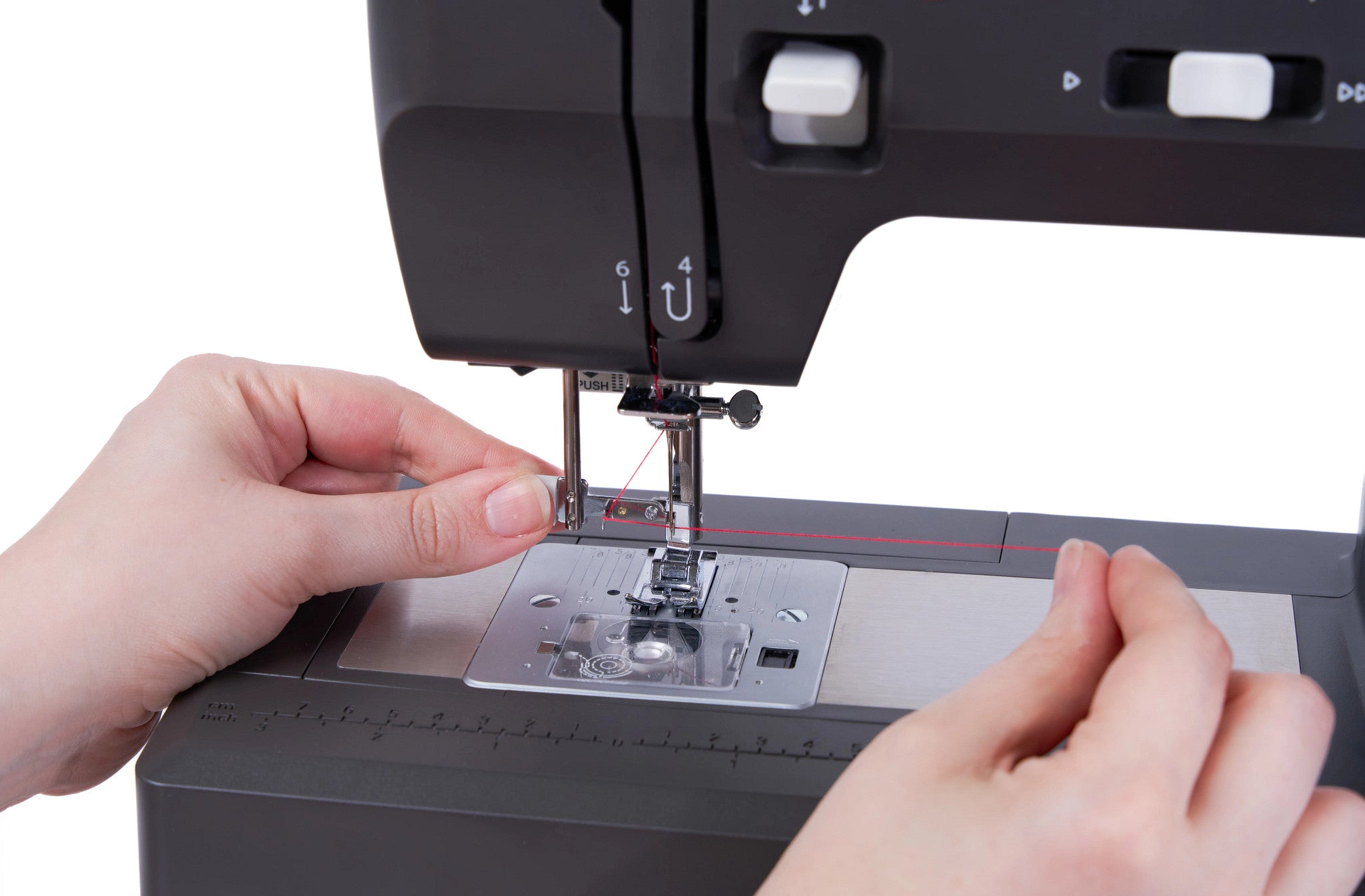 Close-up of a person's hands guiding fabric under the needle of a black sewing machine on a white background.
