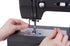 Close-up of a person's hands guiding fabric under the needle of a black sewing machine on a white background.