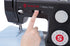 A close-up of a black Singer Heavy Duty sewing machine with a person's finger pressing a button, with a light blue fabric under the needle.