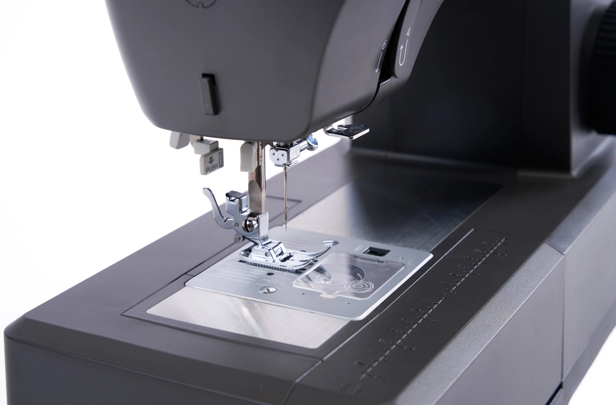 Close-up of a dark gray sewing machine showing the needle area, presser foot, and metal feed dog plate against a white background.
