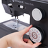 A close-up of a hand turning a large control dial on a black Singer Heavy Duty sewing machine. The dial has a white face with multicolored stitch symbols and a large brown 'S' in the center.