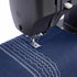 Close-up of a black sewing machine needle plate stitching dark blue fabric with white zigzag and wave stitch patterns.
