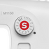 Close-up of a white sewing machine dial with a red circle and white 'S' marking, surrounded by stitch pattern symbols, with 'M1150' printed on the machine body.