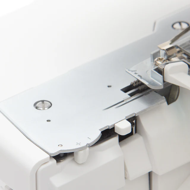 Close-up detail of a white overlocker sewing machine showing the metal presser plate, needle area, and white adjustment knobs.
