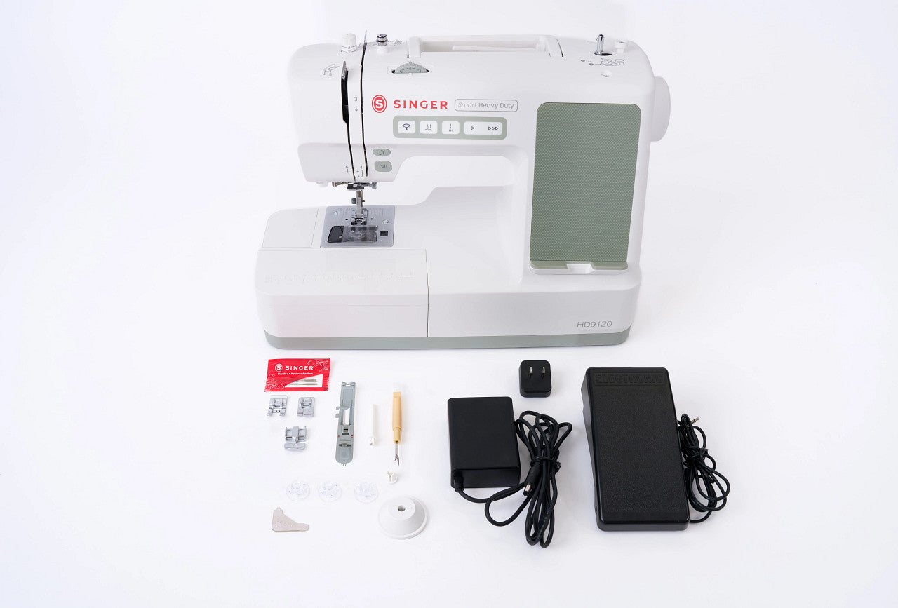 Singer sewing machine set on a white background, including the white and gray sewing machine, black foot pedal, power adapter, presser foot, bobbins, and small accessories.
