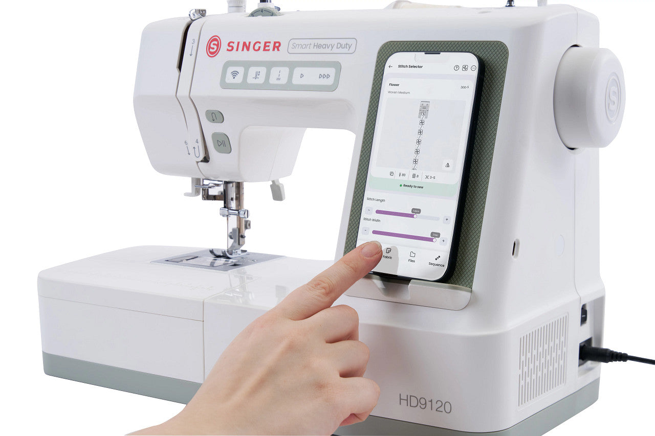 A white Singer smart memory sewing machine with a built-in screen that a finger is touching to display settings, shown on a clean white background.