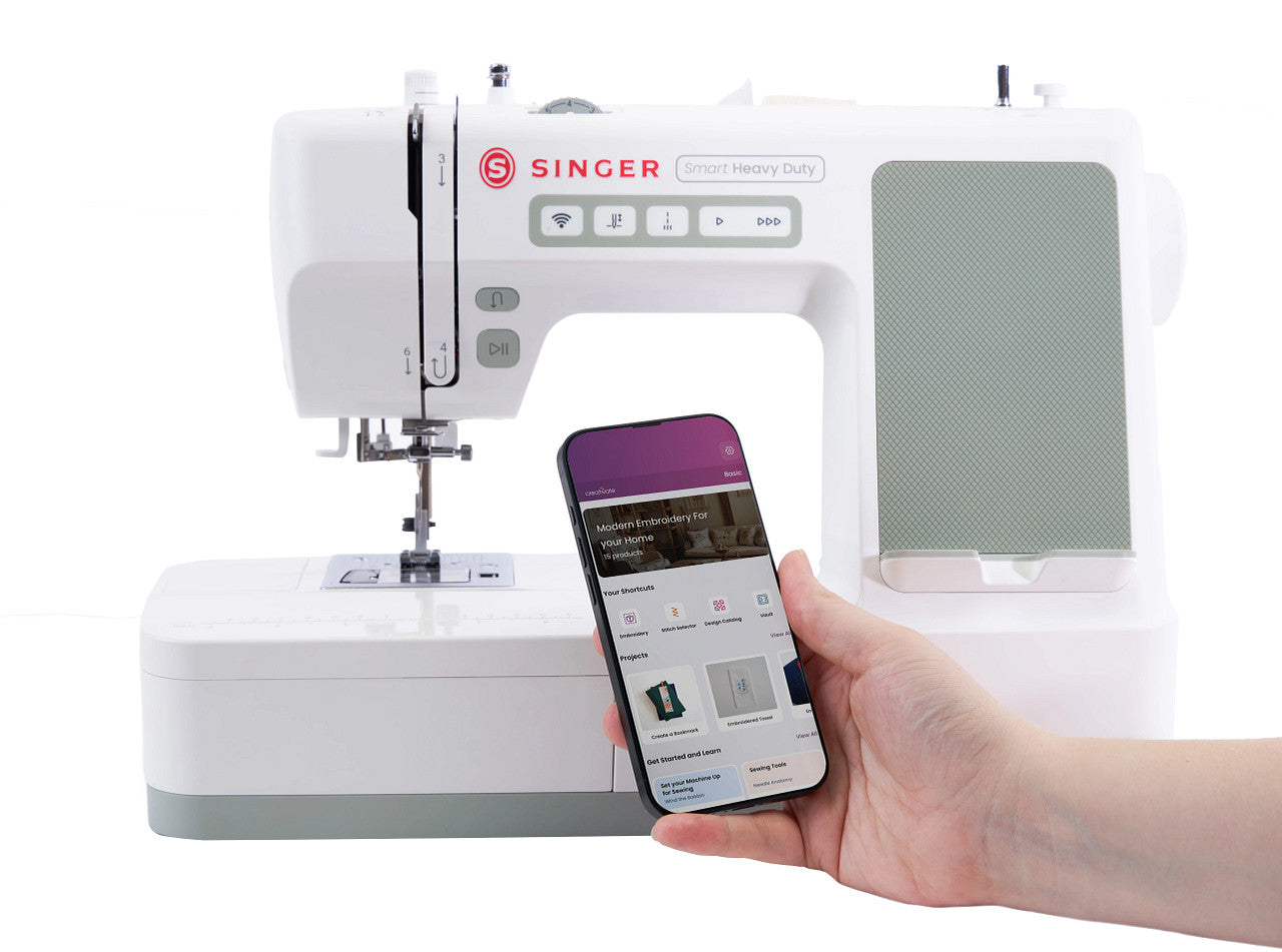 A white Singer sewing machine with a hand holding a smartphone in front of it, shown on a clean white background.