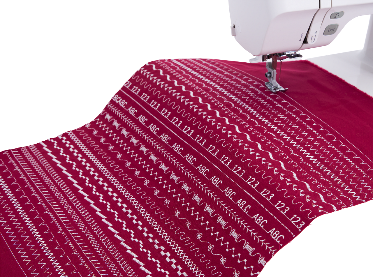 A close-up of a sewing machine needle pressing onto a deep magenta fabric with white geometric and text stitch patterns, shown against a clean white background with part of the white sewing machine visible.