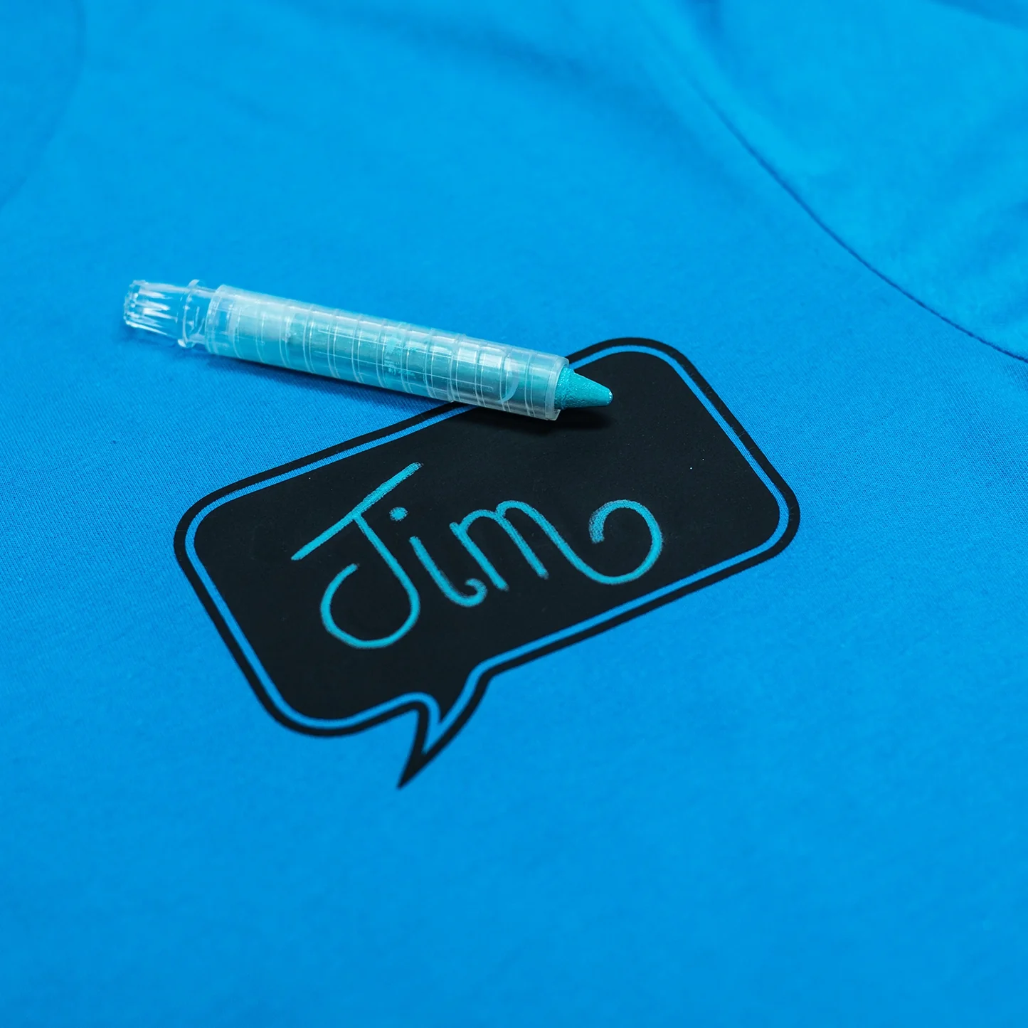 Blue shirt with a black speech bubble graphic and 'Jim' text, accompanied by a marker on a blue background.