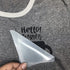 Gray t-shirt with 'Hello! My name is' text held by a hand with a white cone.