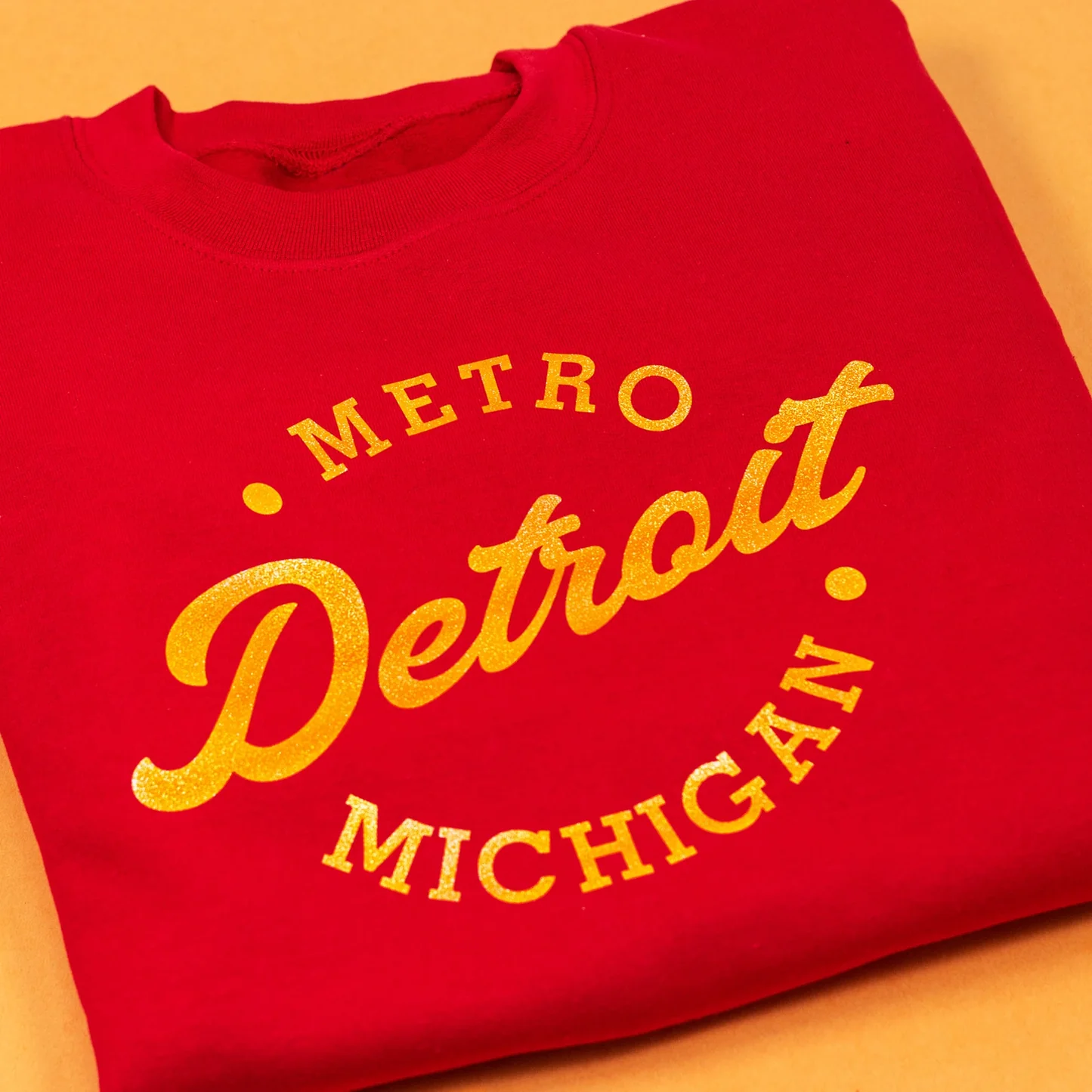Red sweatshirt with 'Metro Detroit Michigan' text in yellow on a wooden surface