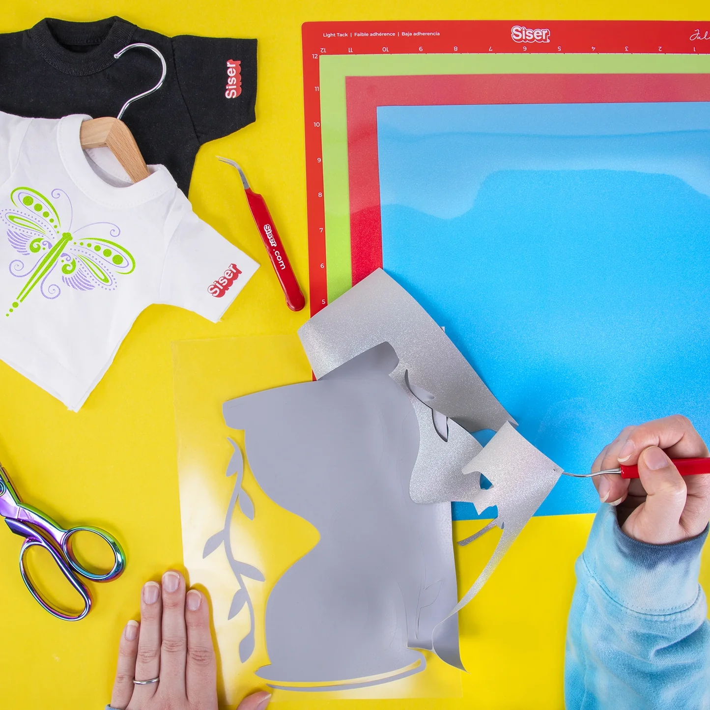 Crafting setup with heat transfer vinyl, cutting mat, and tools on a yellow surface