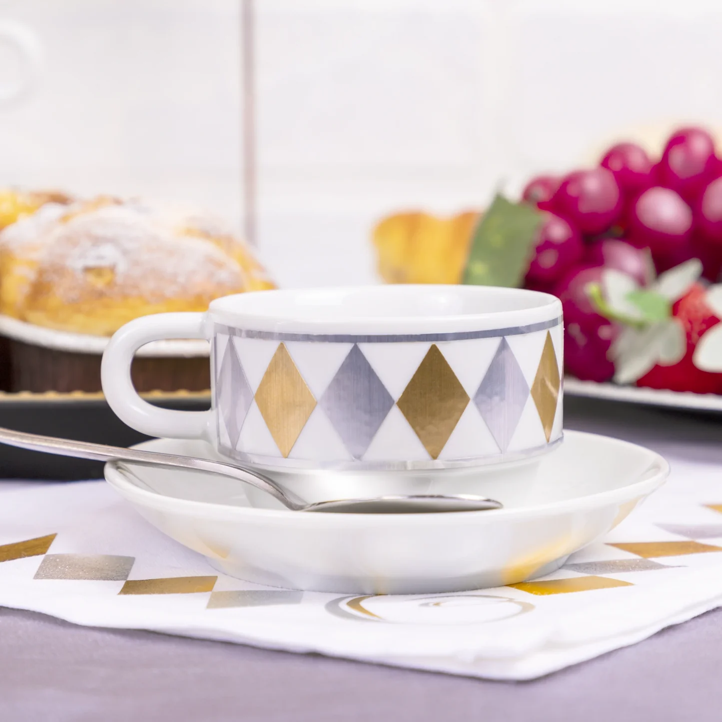 Ceramic cup and saucer with geometric pattern on a table with pastries and fruit in the background