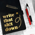 Black notebook with gold text 'write that sh*t down' and a red pen on a white background
