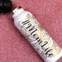 White bottle with gold and black design on a pink glittery background