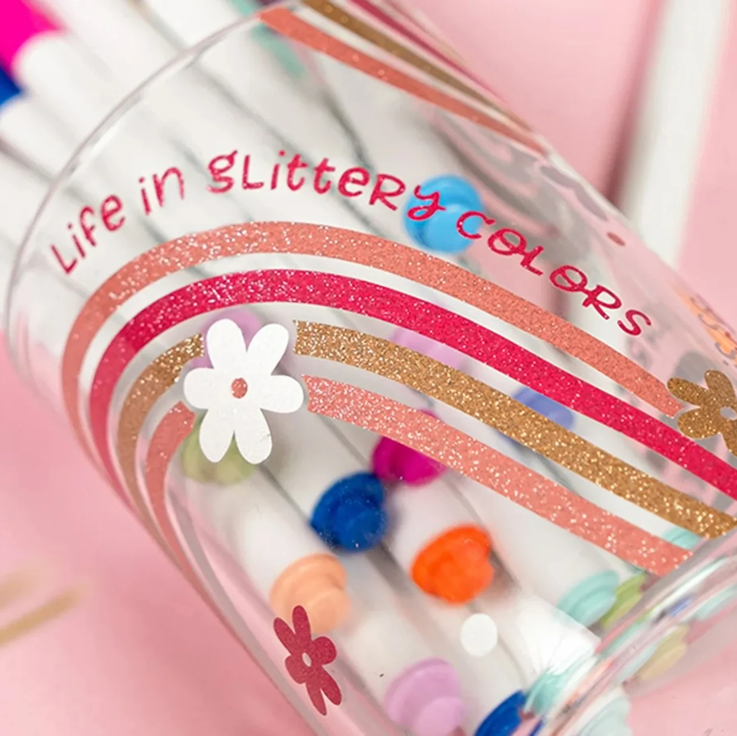 Colorful markers in a transparent holder with decorative elements on a pink background