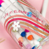 Colorful markers in a transparent holder with decorative elements on a pink background